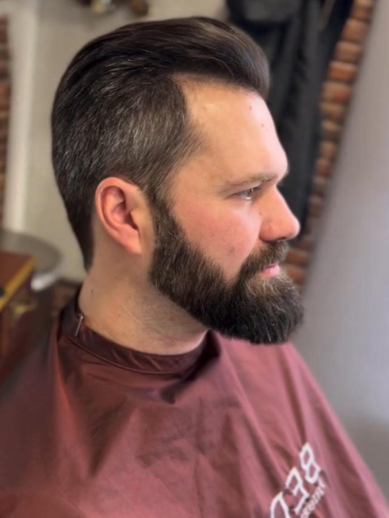 Barbering Mann mit frisch rasiertem und gestyltem Bart und frisiertem Haar im Friseursalon.