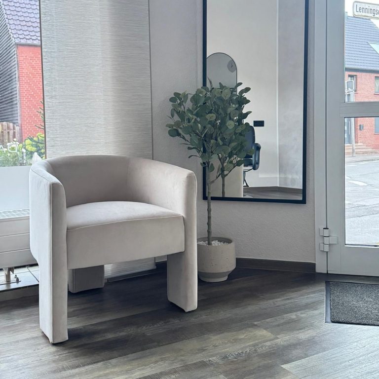 Komm an Hellgrauer Sessel neben einem großen Spiegel und einer kleinen Pflanze in einem modern gestalteten Empfangsbereich.