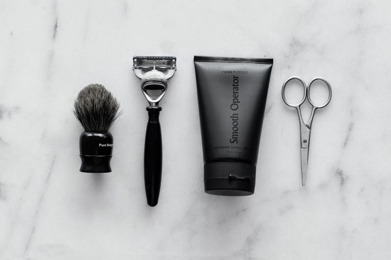 Rasierpinsel Rasierer, Rasierpinsel, Creme und Schere auf einer marmorierten Oberfläche.